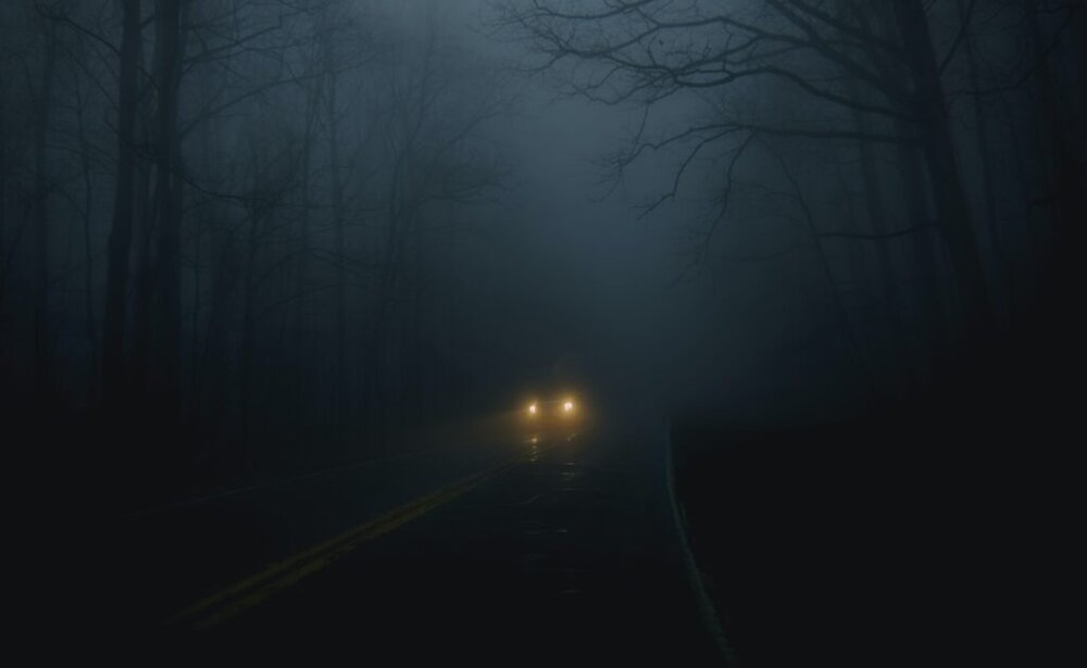 Car driving down a foggy, dimly lit road