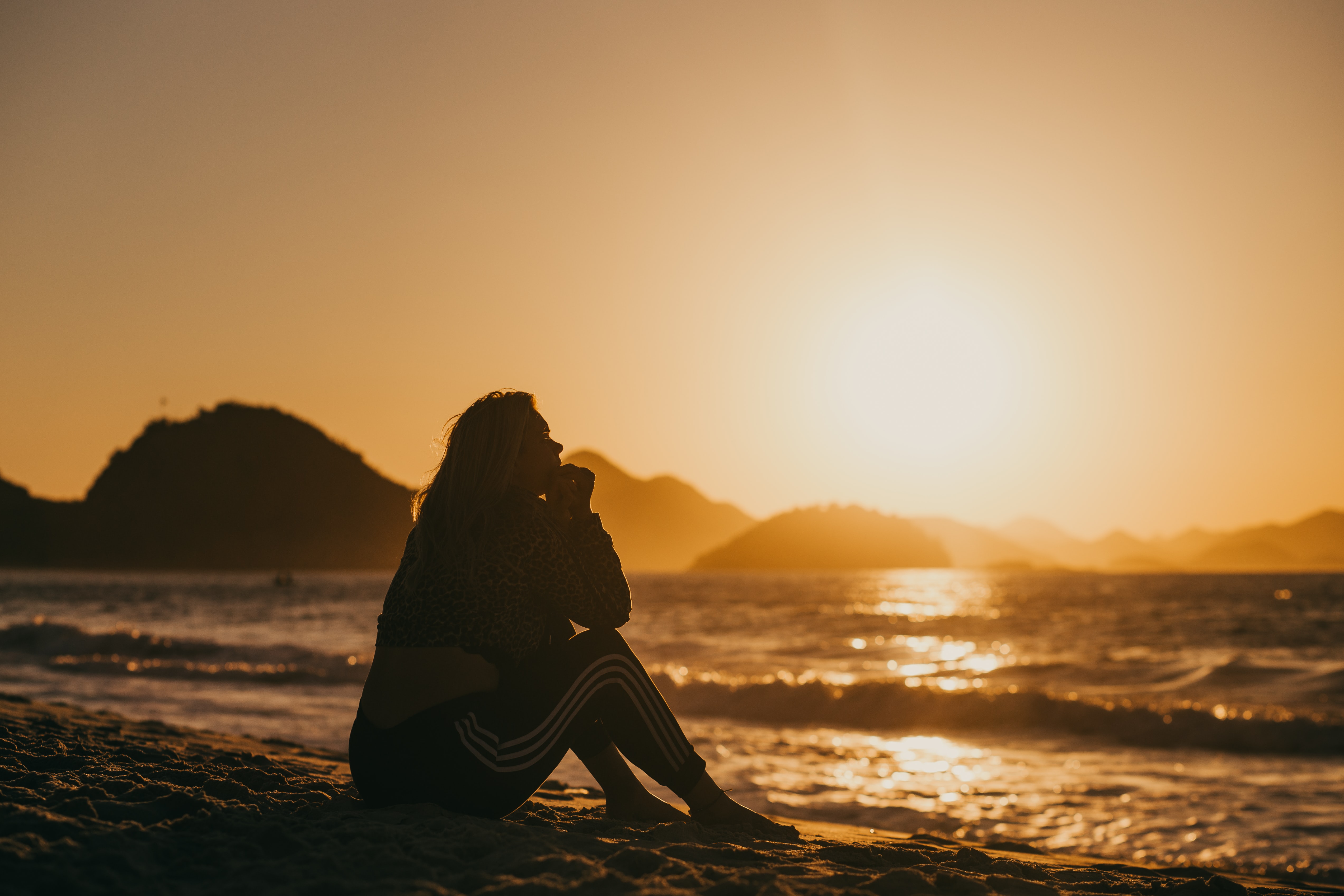 woman sitting on a beach, looking at the ocean